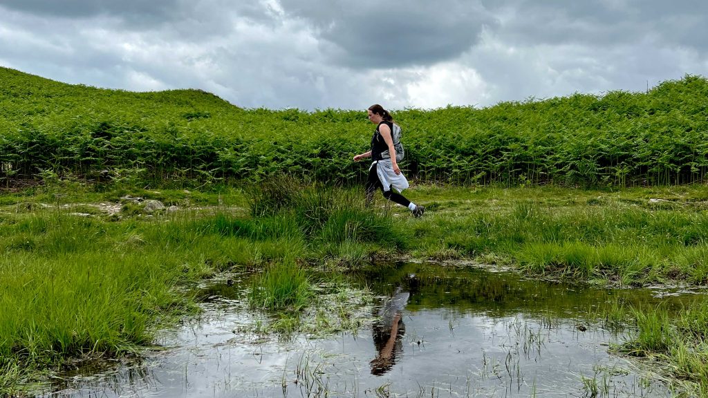 Woman walking, reflection n water around greenery